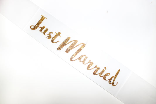 Banda blanca con texto en dorado "Just Married"